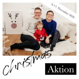 Glückliche Familie beim Weihnachtsfest, sitzend auf einem weißen Teppich, mit festlicher Dekoration und Geschenkverpackungen im Hintergrund.