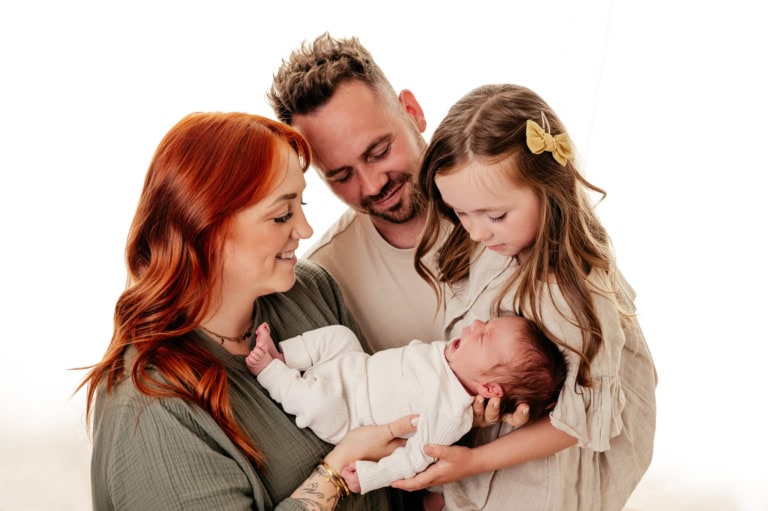 Ein glückliches Familienfoto mit Eltern, Tochter und Neugeborenem, die liebevoll miteinander interagieren.