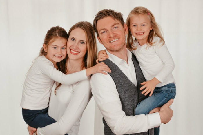 Glückliche Familie mit zwei Kindern, die sich umarmen und lachen vor hellem Hintergrund.