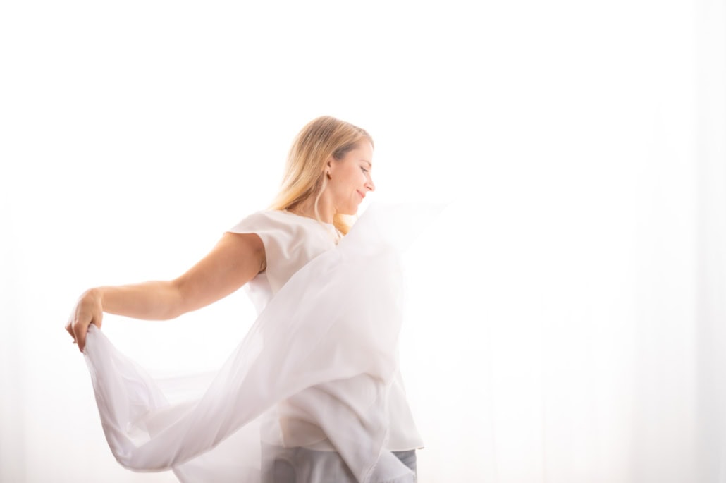 Eine junge Frau in einem weißen Kleid, die im Sonnenlicht vor einem hellen Hintergrund tanzt und Freude zeigt.