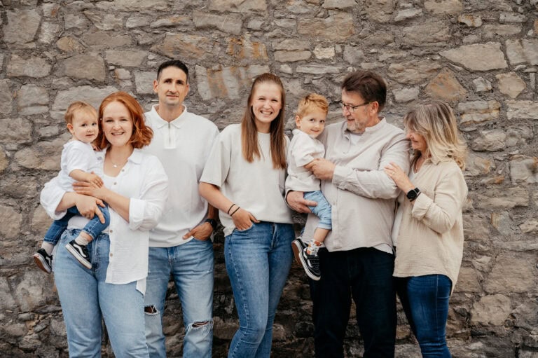 Familienfoto mit fünf Personen vor einer Steinmauer, lachend und in lockerer Kleidung.