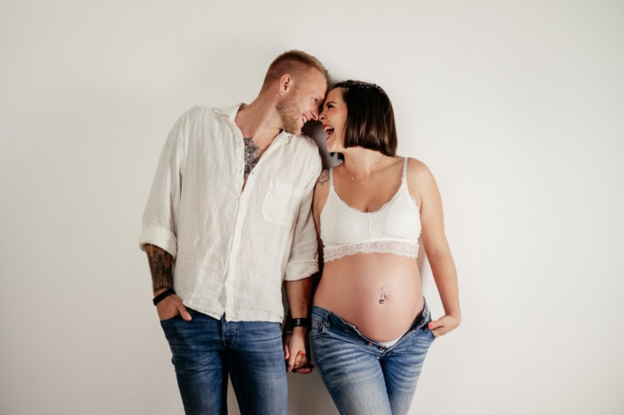 Glückliches Paar, das sich liebevoll anlächelt, während die schwangere Frau ihre Babybauch zeigt.