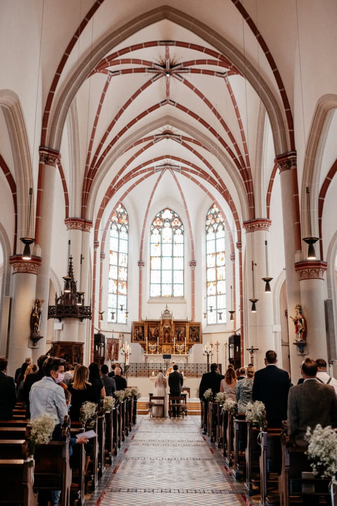 Innenansicht einer gotischen Kirche während einer Zeremonie mit Hochzeitsgästen, die an den Bänken sitzen und beten.