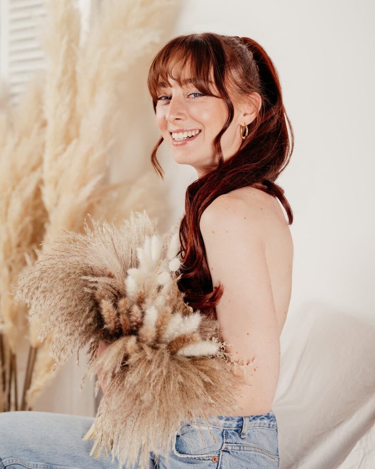 Warme, natürliche Dekoration mit getrockneten Blumen und Pampasgras, Frau mit rotem Haar, lächelnd, im Wohnzimmer sitzend, entspannte Atmosphäre, modernes Interior, Lifestyle-Fotografie.